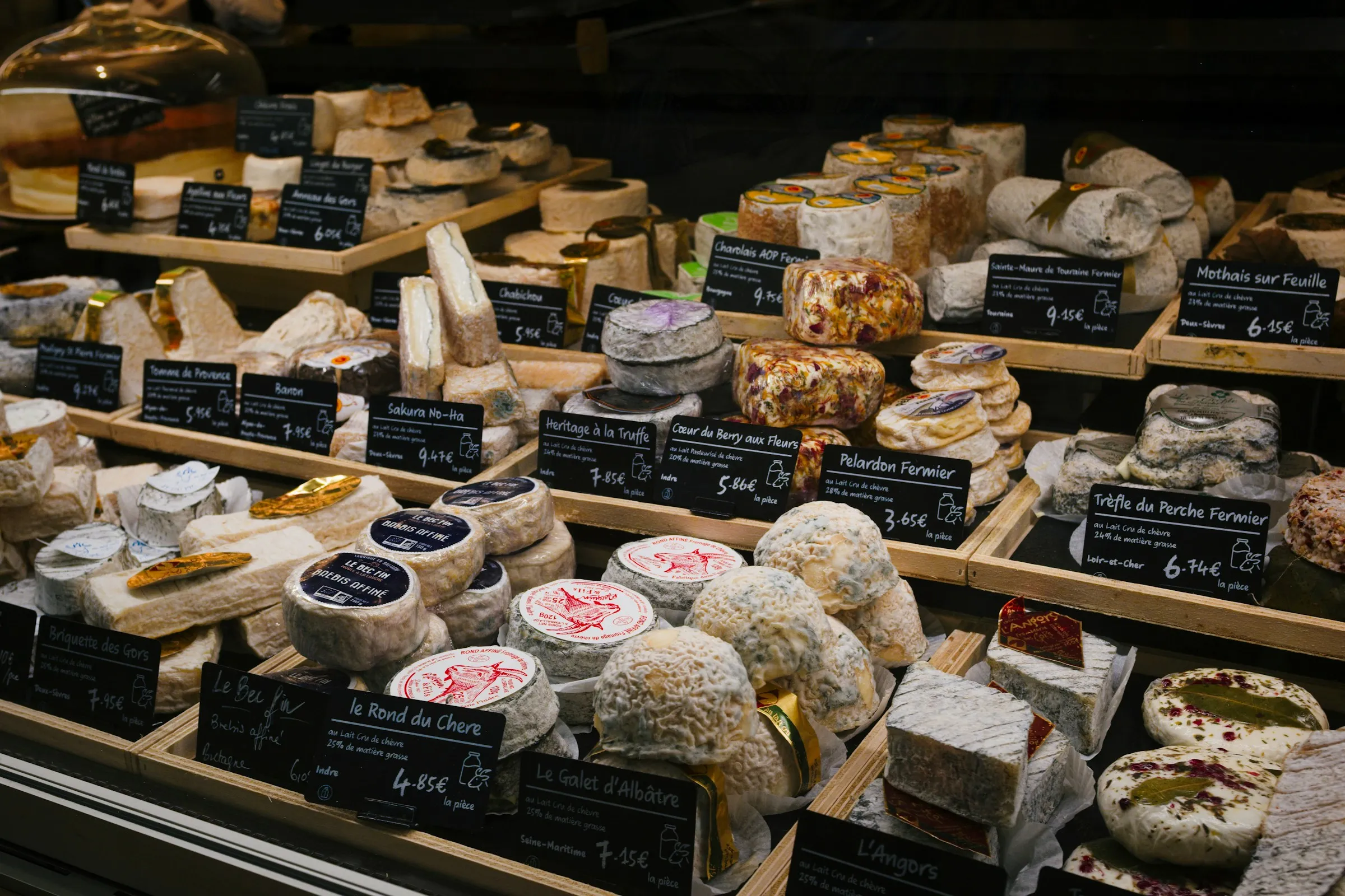 Vitrine de fromagerie — étagères en bois, chaque pièce avec un cartel nom et prix, comme un catalogue lisible